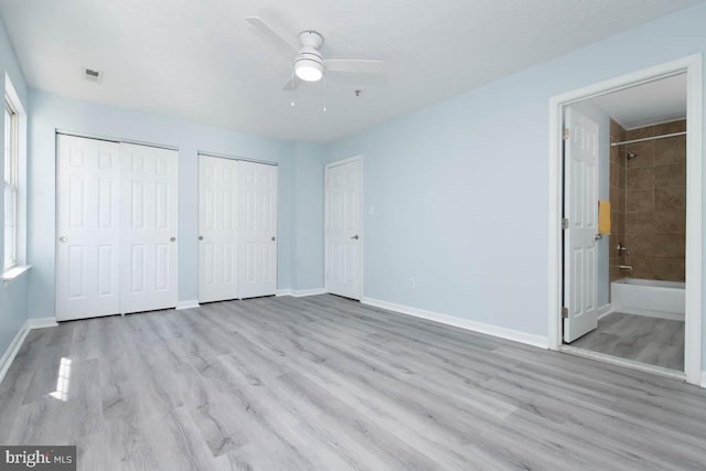 unfurnished bedroom with baseboards, ensuite bath, ceiling fan, wood finished floors, and multiple closets