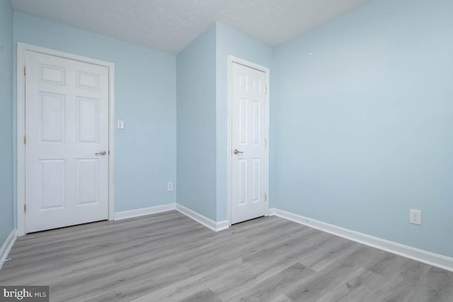 unfurnished bedroom featuring a textured ceiling, baseboards, and wood finished floors