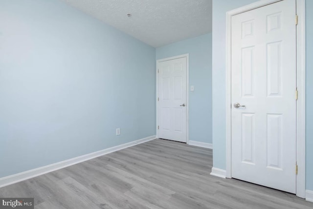 unfurnished bedroom with a textured ceiling, baseboards, and wood finished floors