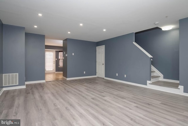 unfurnished living room with stairs, wood finished floors, visible vents, and baseboards