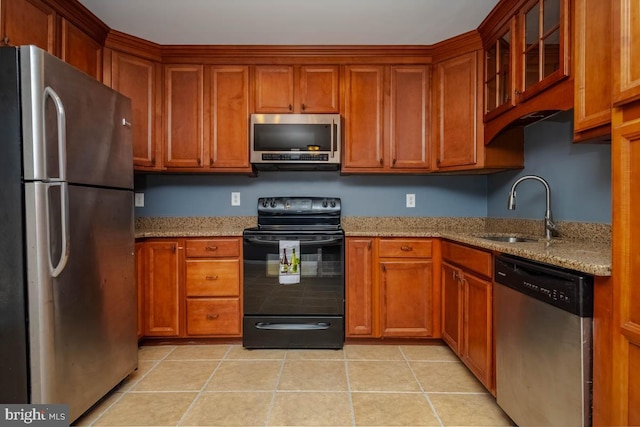 kitchen featuring light tile patterned floors, stainless steel appliances, brown cabinetry, a sink, and light stone countertops