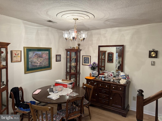 dining space featuring light wood-type flooring, visible vents, a notable chandelier, and a textured ceiling