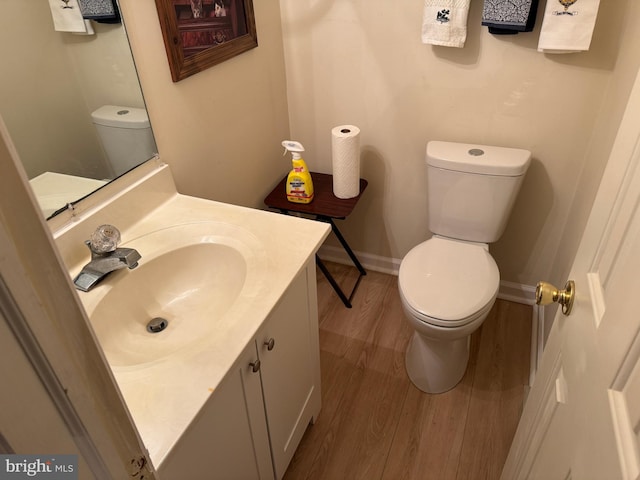 half bathroom with baseboards, vanity, toilet, and wood finished floors