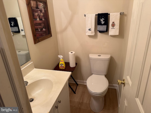 half bathroom featuring toilet, wood finished floors, vanity, and baseboards