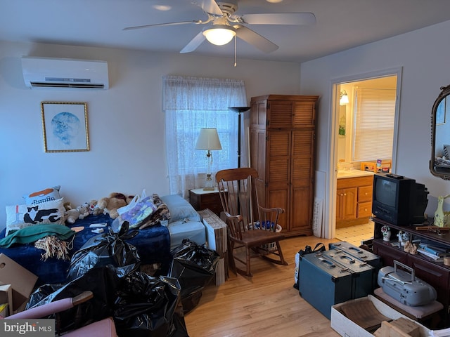 bedroom with an AC wall unit, light wood finished floors, connected bathroom, and a ceiling fan