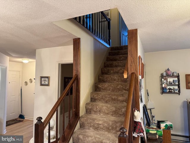 staircase featuring baseboards, a textured ceiling, baseboard heating, and wood finished floors