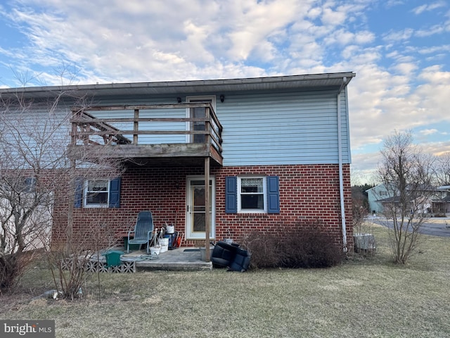 back of house featuring a balcony, a patio area, a yard, and brick siding