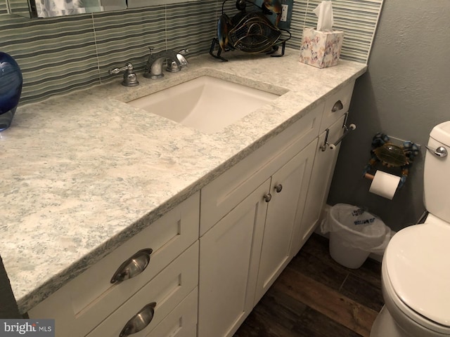 bathroom with decorative backsplash, a textured wall, toilet, wood finished floors, and vanity