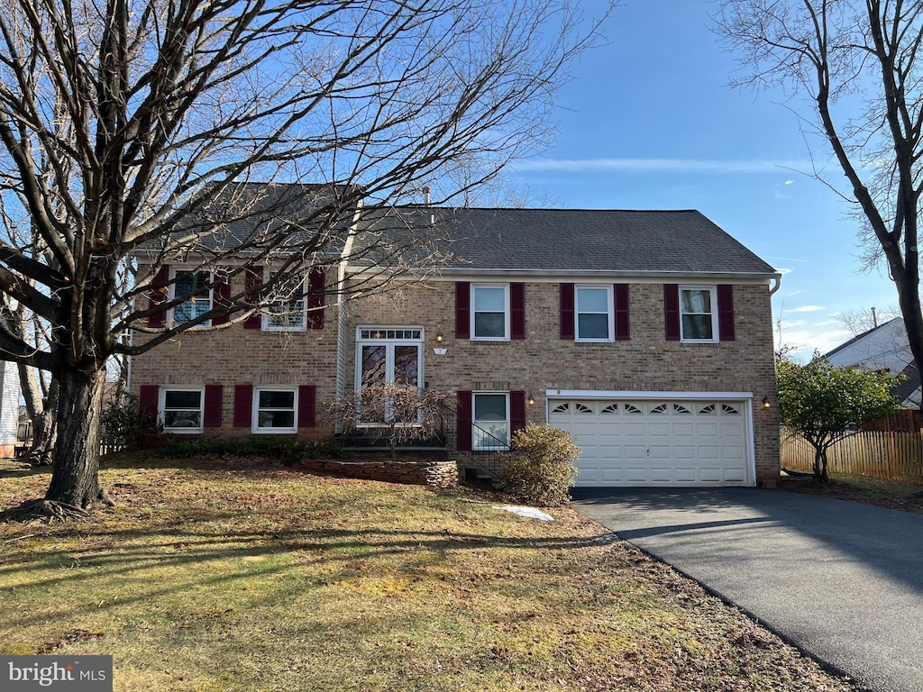 raised ranch with a garage, brick siding, fence, driveway, and a front yard