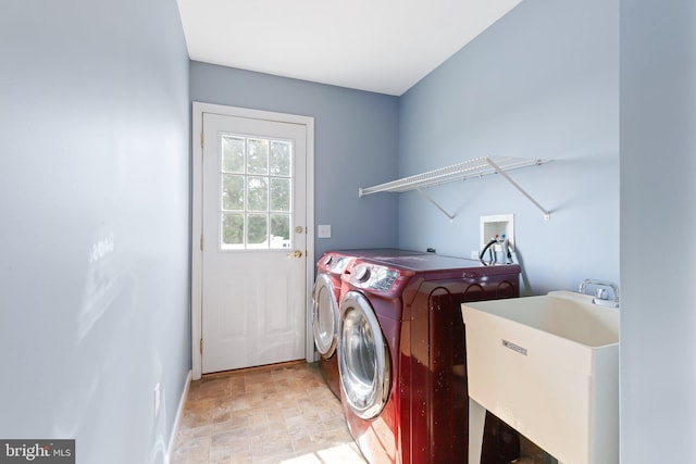 clothes washing area featuring laundry area, baseboards, stone finish flooring, washing machine and dryer, and a sink