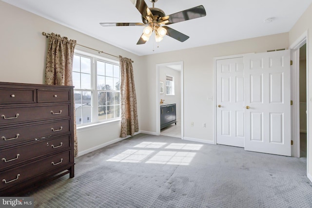 unfurnished bedroom featuring a closet, light colored carpet, ensuite bathroom, a ceiling fan, and baseboards