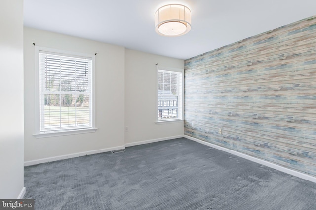 spare room featuring carpet floors, an accent wall, visible vents, and plenty of natural light