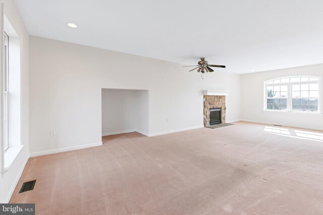 unfurnished living room with ceiling fan, a stone fireplace, visible vents, and baseboards