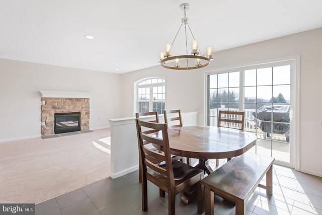 carpeted dining space featuring tile patterned flooring, baseboards, a notable chandelier, and a stone fireplace