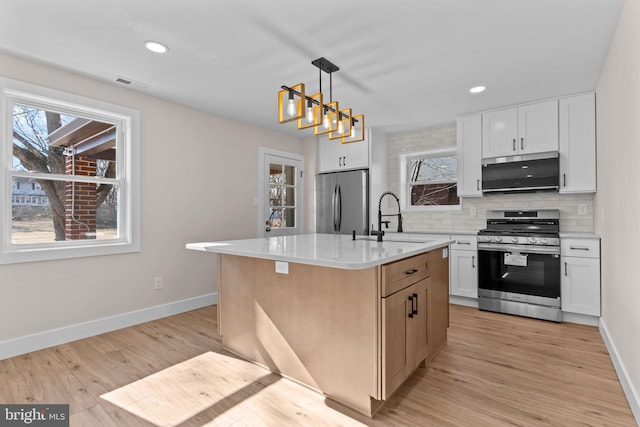 kitchen featuring decorative light fixtures, a center island with sink, stainless steel appliances, white cabinets, and a sink