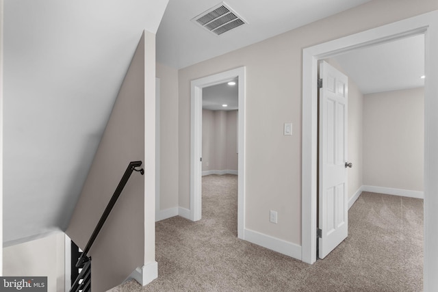 hallway featuring light carpet, baseboards, visible vents, and an upstairs landing