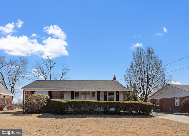 ranch-style home with roof with shingles, brick siding, and a chimney