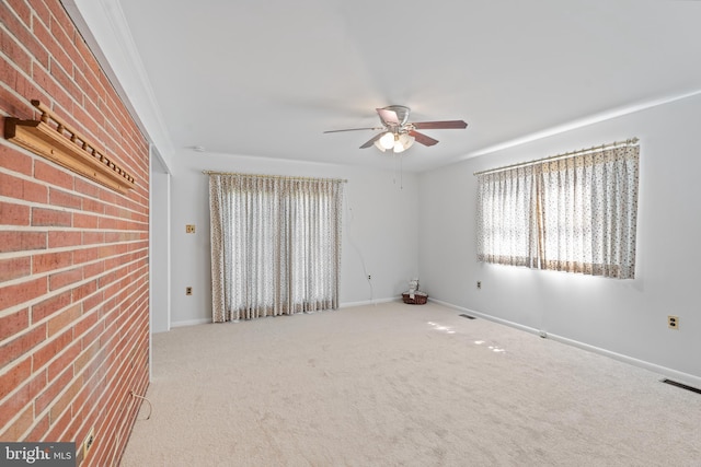 empty room with carpet floors, visible vents, ceiling fan, brick wall, and baseboards