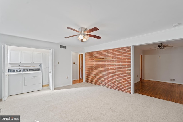 unfurnished living room featuring light colored carpet, visible vents, a ceiling fan, brick wall, and washer and dryer