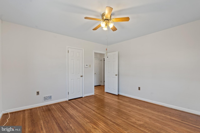 unfurnished room featuring visible vents, wood finished floors, a ceiling fan, and baseboards