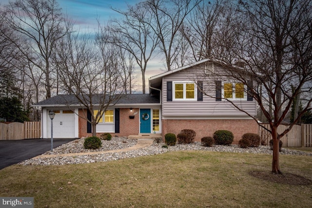 split level home featuring driveway, brick siding, an attached garage, fence, and a front yard