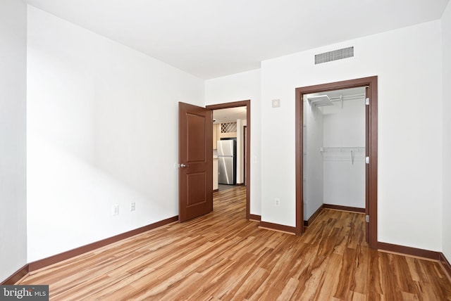 unfurnished bedroom featuring visible vents, light wood finished floors, freestanding refrigerator, and baseboards