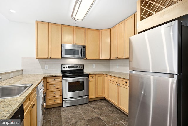 kitchen with a sink, appliances with stainless steel finishes, backsplash, light stone countertops, and light brown cabinetry