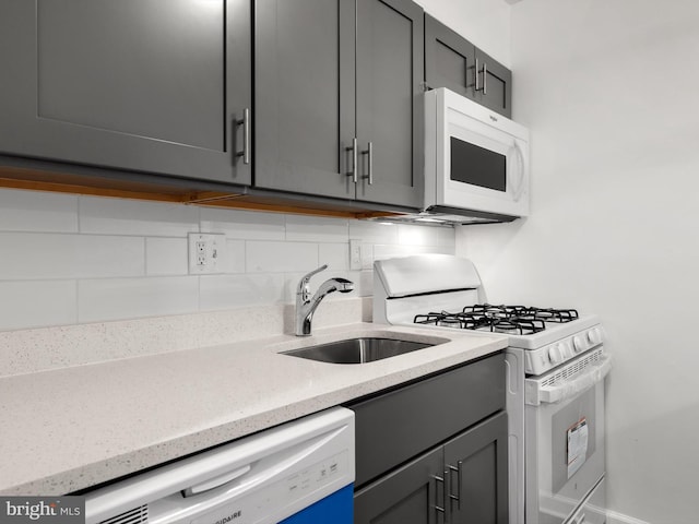 kitchen featuring white appliances, decorative backsplash, light stone countertops, gray cabinets, and a sink