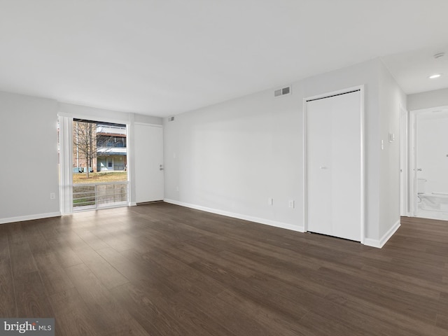 spare room featuring dark wood-type flooring, visible vents, and baseboards