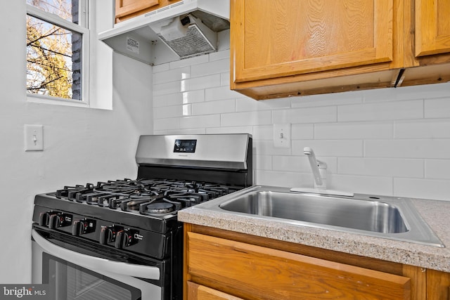 kitchen with decorative backsplash, light countertops, under cabinet range hood, a sink, and gas stove