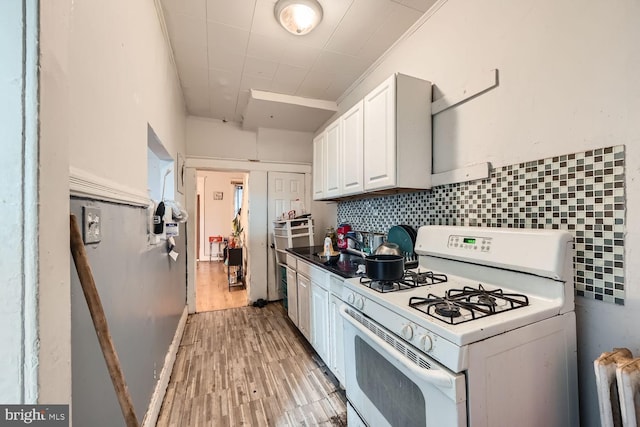 kitchen featuring dark countertops, backsplash, white cabinets, light wood-type flooring, and white range with gas stovetop
