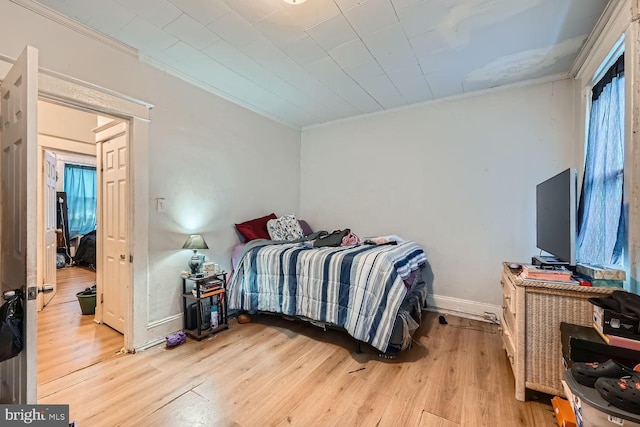 bedroom featuring light wood finished floors, baseboards, and crown molding