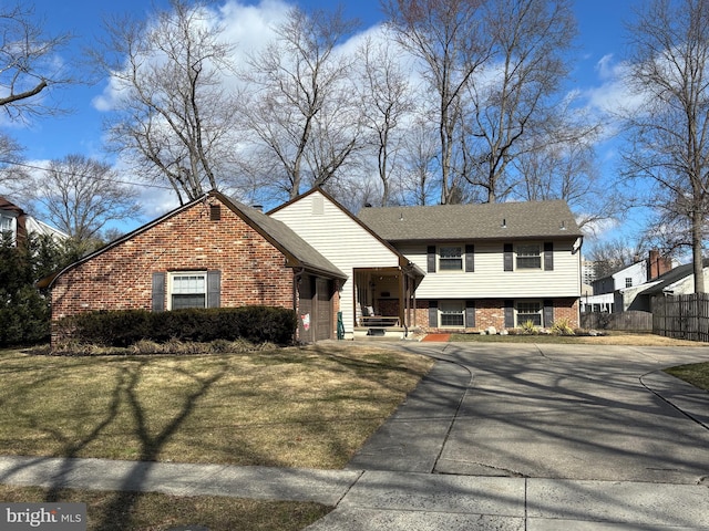 tri-level home featuring concrete driveway, brick siding, a front yard, and fence