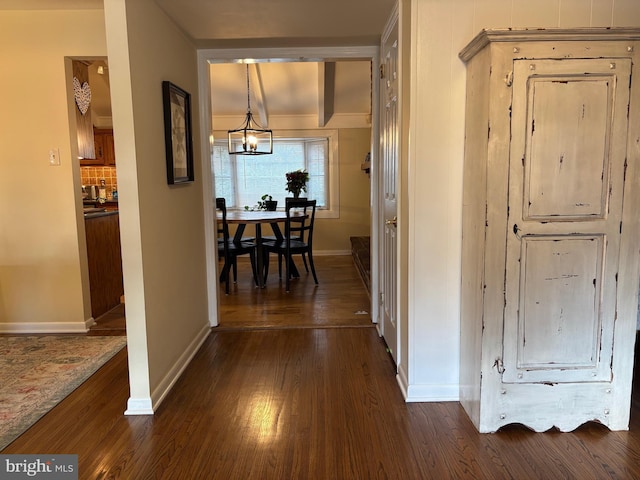 hallway with dark wood-style floors, a chandelier, and baseboards