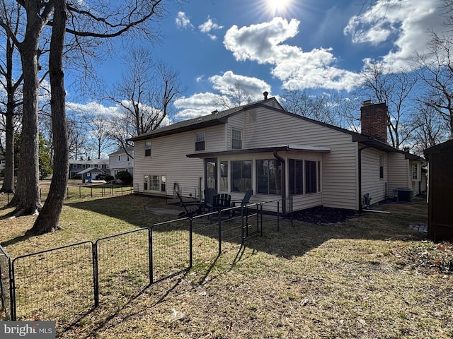 back of property with a chimney, central air condition unit, a lawn, a sunroom, and a fenced backyard