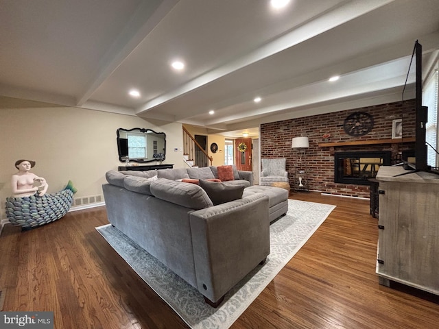 living room featuring dark wood finished floors, brick wall, beamed ceiling, stairs, and a fireplace