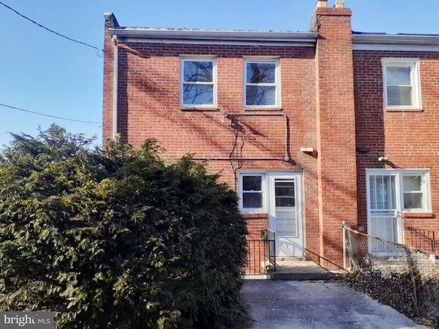 rear view of house featuring a chimney, fence, and brick siding