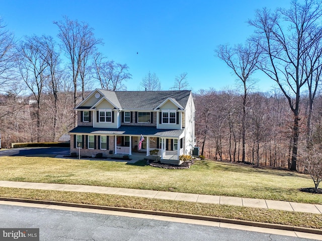 view of front of house with a forest view, a porch, and a front yard