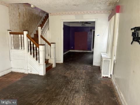 hallway with stairway, a textured ceiling, baseboards, and wood finished floors