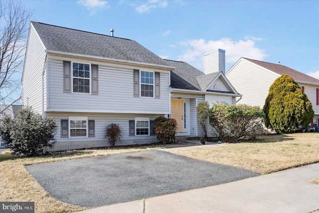 tri-level home with a shingled roof, a chimney, and a front yard