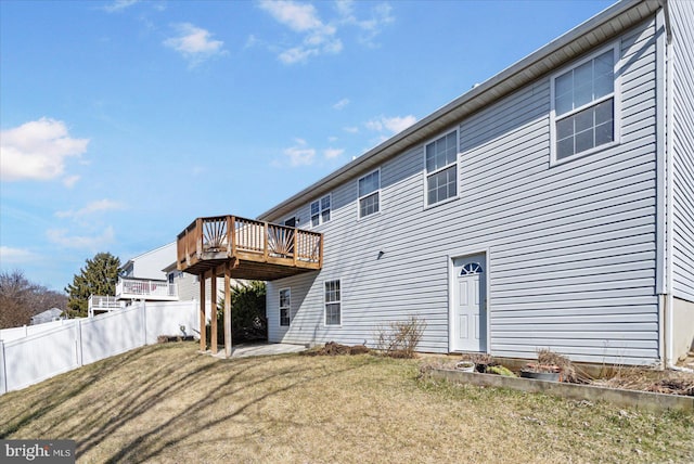 rear view of property featuring a lawn, a wooden deck, and fence