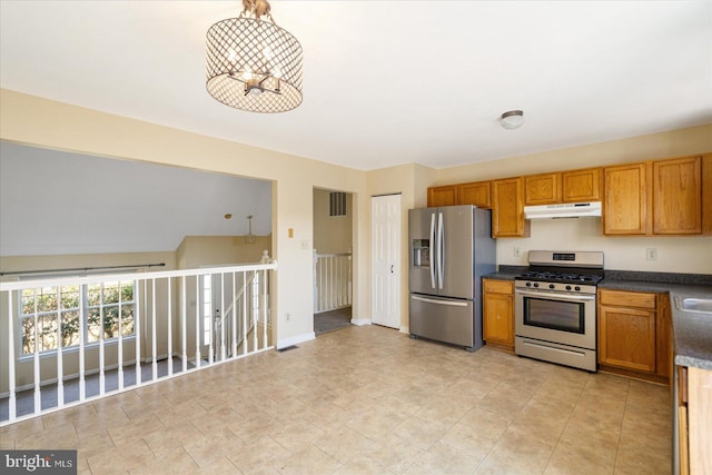 kitchen featuring dark countertops, appliances with stainless steel finishes, brown cabinetry, under cabinet range hood, and baseboards