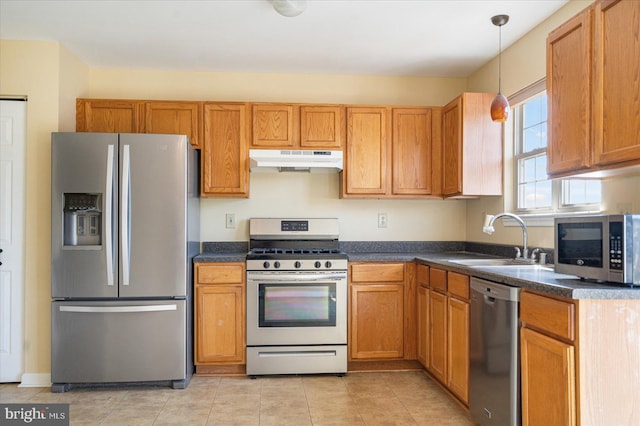 kitchen with under cabinet range hood, a sink, appliances with stainless steel finishes, dark countertops, and pendant lighting