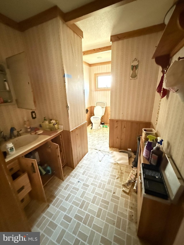 interior space with wallpapered walls, a textured ceiling, brick floor, and a sink