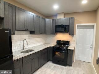 kitchen with decorative backsplash, light countertops, a sink, and black appliances