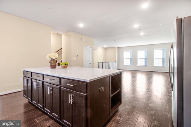 kitchen with dark brown cabinetry, dark wood finished floors, a kitchen island, freestanding refrigerator, and light countertops