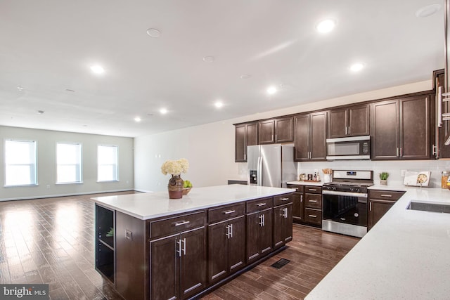 kitchen with dark wood-style flooring, dark brown cabinets, appliances with stainless steel finishes, light countertops, and a center island