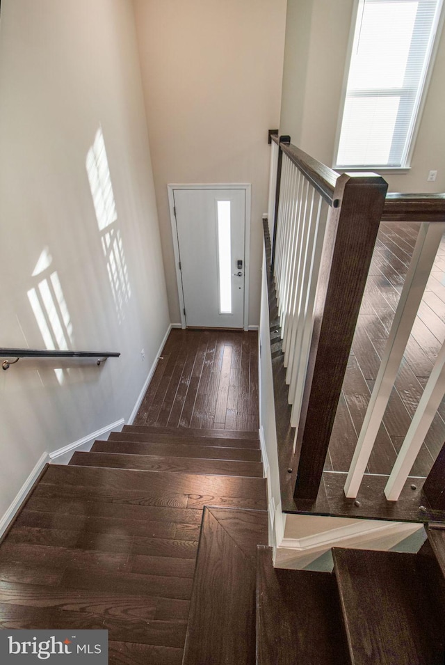 staircase featuring wood-type flooring, a towering ceiling, and baseboards