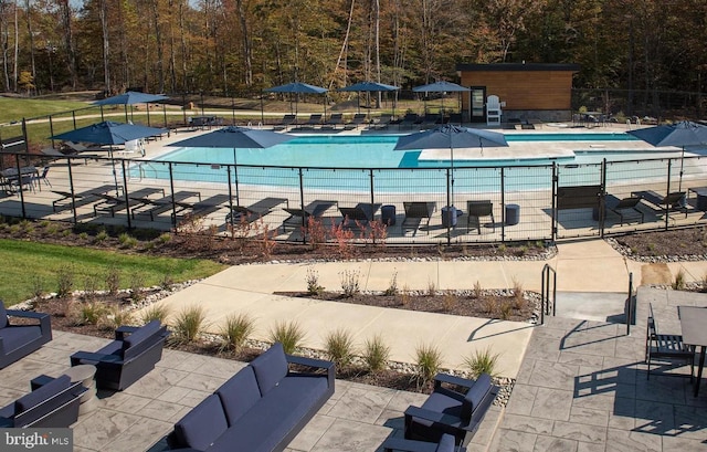 community pool featuring a patio, a view of trees, and fence