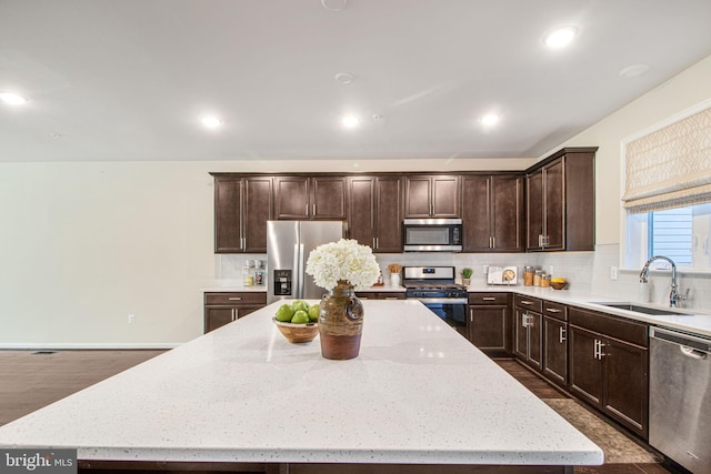 kitchen with a kitchen island, appliances with stainless steel finishes, a sink, dark brown cabinets, and backsplash